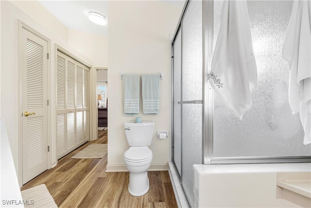 bathroom with toilet, a shower with shower door, and hardwood / wood-style flooring