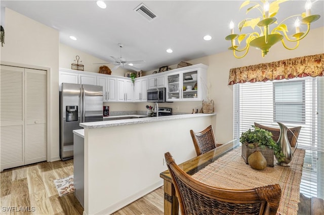 kitchen featuring light hardwood / wood-style floors, appliances with stainless steel finishes, hanging light fixtures, vaulted ceiling, and white cabinets