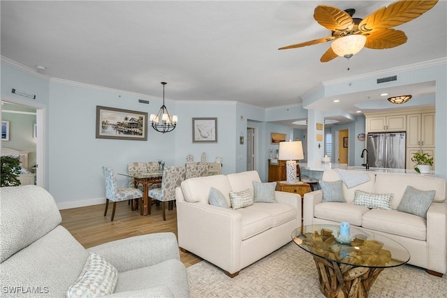 living room featuring sink, light wood-type flooring, ceiling fan with notable chandelier, and ornamental molding