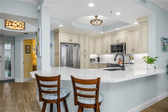 kitchen featuring a kitchen breakfast bar, kitchen peninsula, cream cabinetry, a tray ceiling, and stainless steel appliances