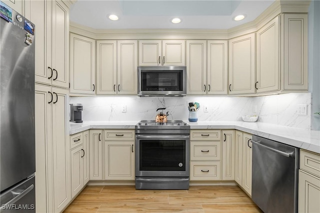 kitchen with cream cabinetry, light hardwood / wood-style flooring, appliances with stainless steel finishes, and decorative backsplash