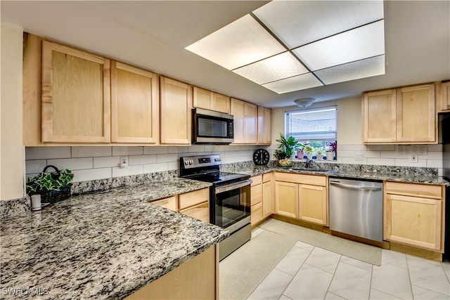 kitchen with light stone countertops, backsplash, appliances with stainless steel finishes, and light brown cabinets