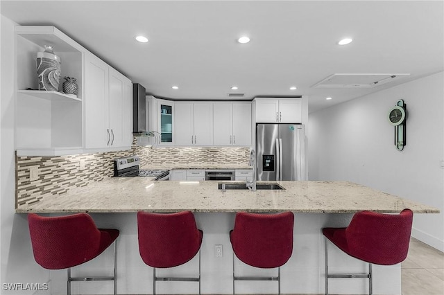 kitchen with white cabinetry, appliances with stainless steel finishes, wall chimney range hood, and light stone counters