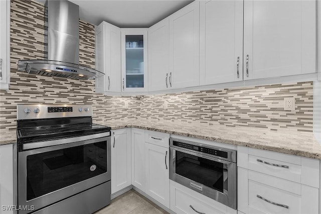 kitchen with stainless steel electric range oven, tasteful backsplash, white cabinets, light stone counters, and wall chimney exhaust hood