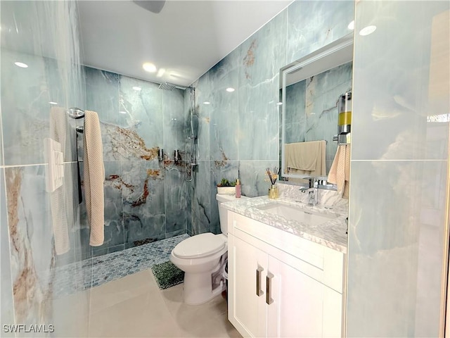 bathroom with tiled shower, tile patterned floors, toilet, tile walls, and vanity