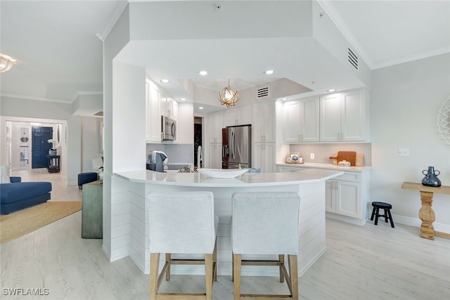 kitchen with white cabinets, appliances with stainless steel finishes, tasteful backsplash, kitchen peninsula, and a breakfast bar