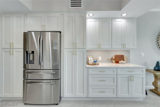 kitchen with stainless steel refrigerator with ice dispenser, white cabinets, and tasteful backsplash