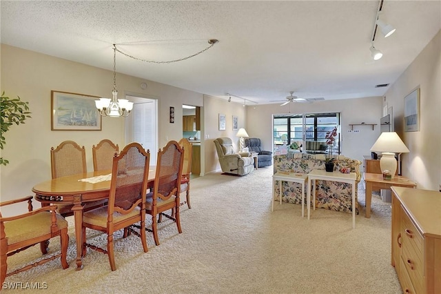 dining space with ceiling fan with notable chandelier, light colored carpet, a textured ceiling, and rail lighting