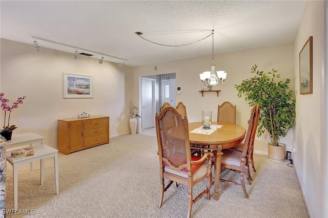 dining area featuring a notable chandelier, light colored carpet, rail lighting, and a textured ceiling