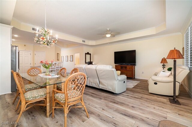 dining space with ceiling fan with notable chandelier, a tray ceiling, light hardwood / wood-style flooring, and ornamental molding