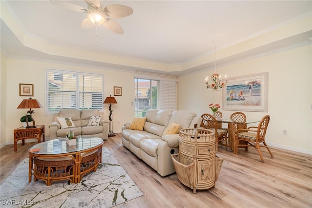 living room with ceiling fan with notable chandelier, a tray ceiling, light hardwood / wood-style flooring, and ornamental molding