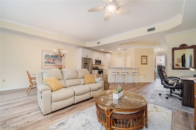 living room with light wood-type flooring, crown molding, ceiling fan with notable chandelier, and a tray ceiling