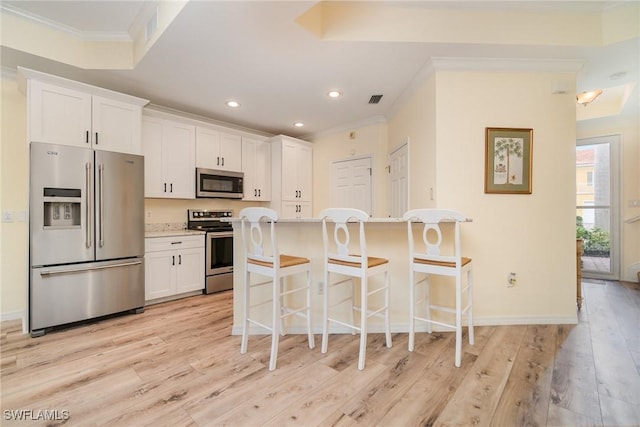 kitchen with appliances with stainless steel finishes, a kitchen bar, white cabinetry, an island with sink, and light hardwood / wood-style floors