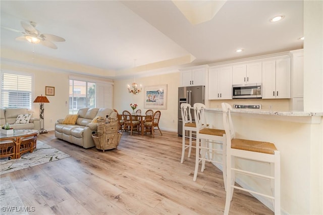 kitchen featuring white cabinetry, stainless steel appliances, a raised ceiling, a kitchen breakfast bar, and ceiling fan with notable chandelier