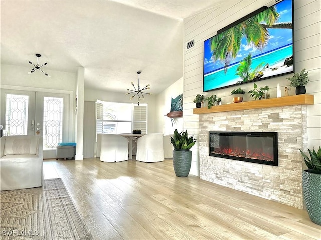 living room featuring french doors, plenty of natural light, a stone fireplace, and light wood-type flooring