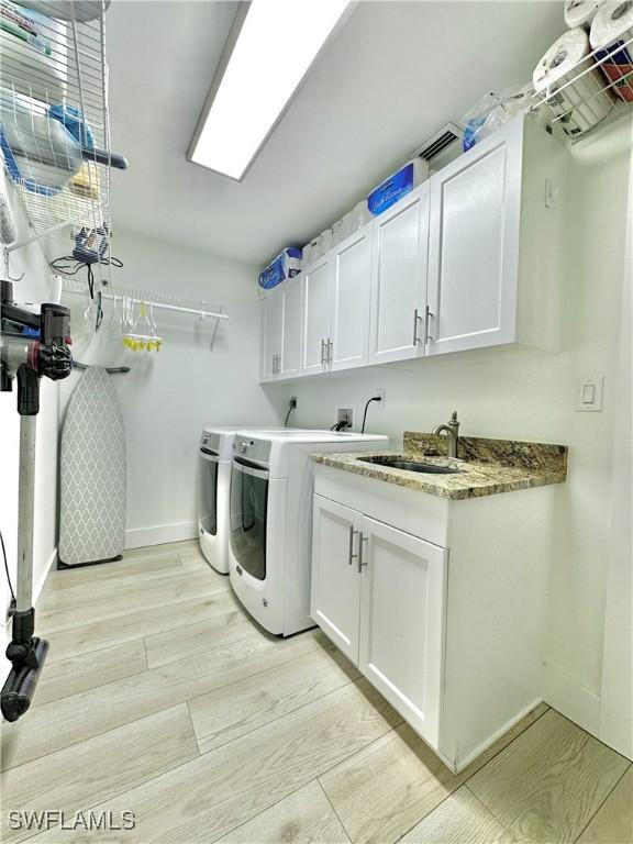 9553 Campbell Cir, Naples, FL 34109 - laundry area with baseboards, separate washer and dryer, a sink, light wood-style flooring, and cabinet space