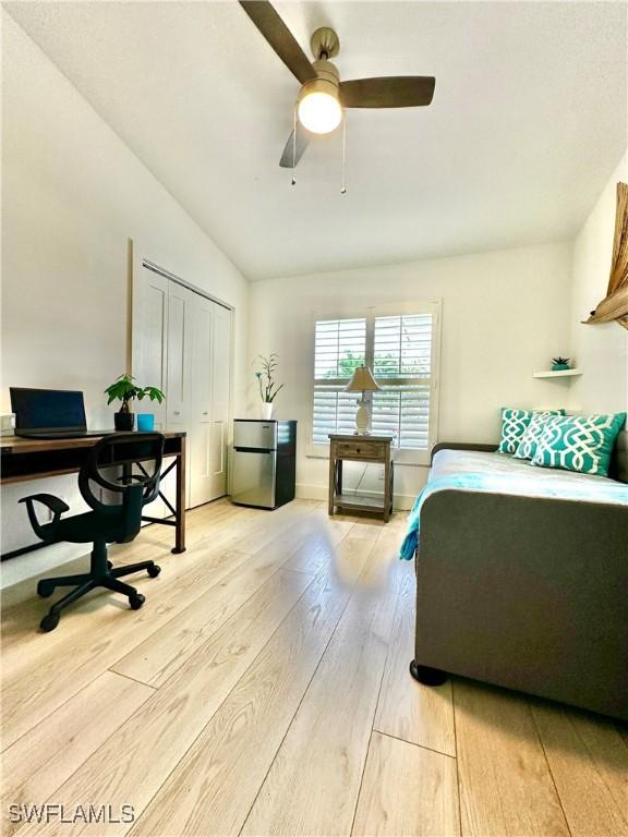 bedroom featuring lofted ceiling, light hardwood / wood-style flooring, stainless steel refrigerator, a closet, and ceiling fan