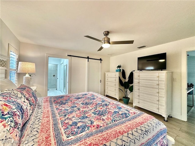 bedroom featuring ceiling fan, a barn door, ensuite bath, and light hardwood / wood-style flooring