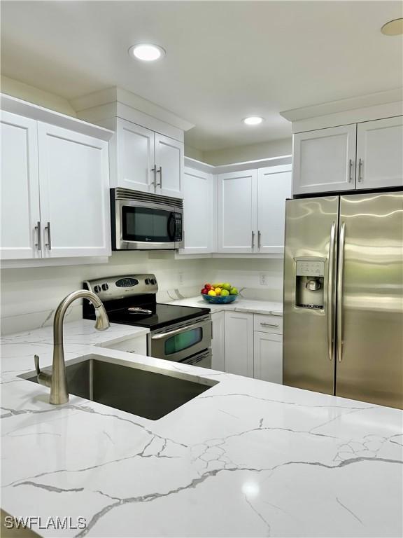 kitchen with white cabinetry, stainless steel appliances, light stone countertops, and sink