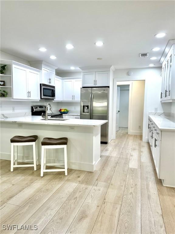 kitchen with a breakfast bar, kitchen peninsula, stainless steel appliances, light hardwood / wood-style floors, and white cabinets