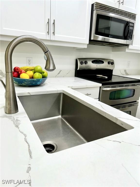 details featuring white cabinetry, light stone counters, and appliances with stainless steel finishes