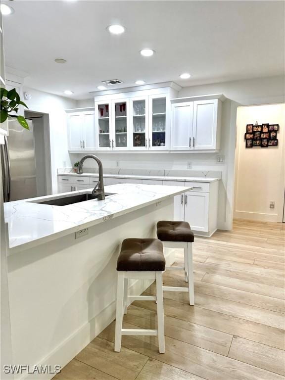 kitchen with white cabinetry, light stone counters, a breakfast bar, and light wood-type flooring