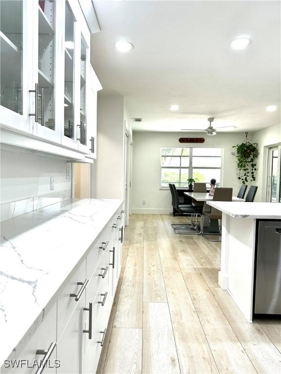 kitchen with white cabinetry, light stone countertops, dishwasher, and light hardwood / wood-style floors