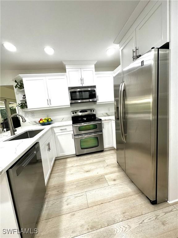 kitchen with sink, white cabinetry, stainless steel appliances, light stone countertops, and light wood-type flooring