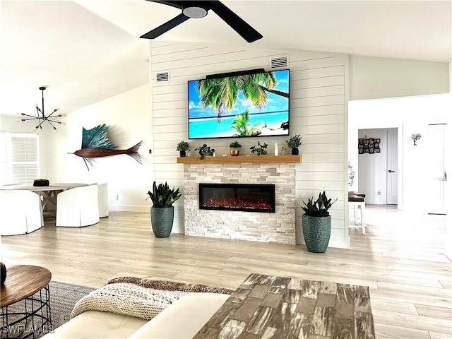 living room with ceiling fan with notable chandelier, a fireplace, and light wood-type flooring