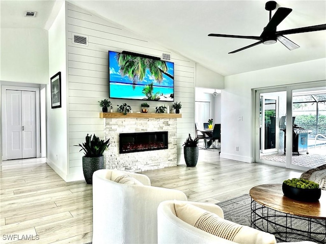 living room with ceiling fan, a stone fireplace, and light wood-type flooring