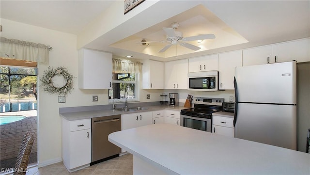 kitchen featuring sink, appliances with stainless steel finishes, white cabinetry, a tray ceiling, and a wealth of natural light