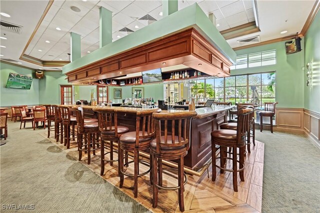 bar featuring light colored carpet, ornamental molding, and a tray ceiling