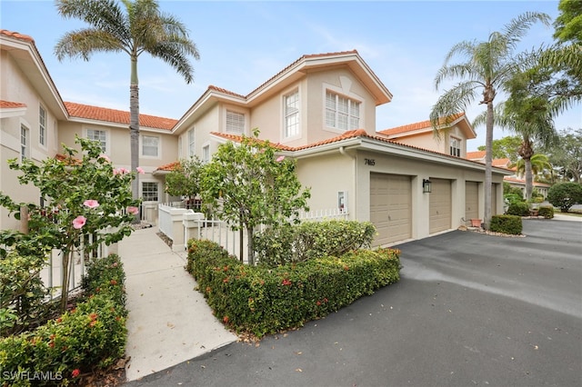 view of front facade with aphalt driveway, a tile roof, stucco siding, fence, and a garage