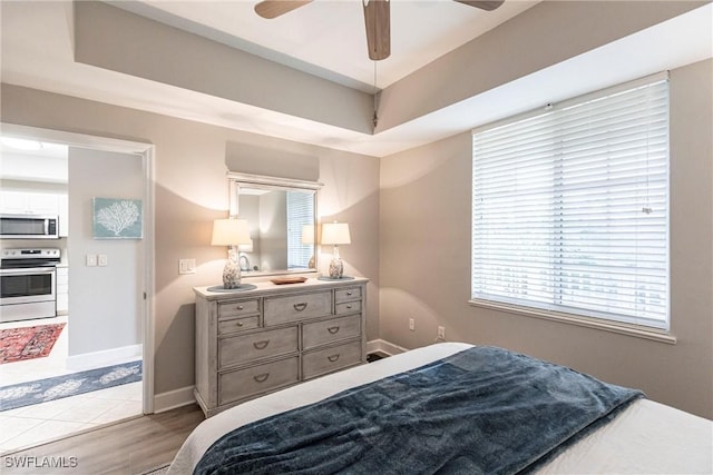 bedroom with ceiling fan, a tray ceiling, and light hardwood / wood-style flooring