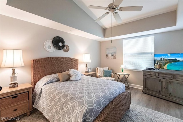 bedroom featuring ceiling fan, lofted ceiling, light wood-type flooring, and a tray ceiling