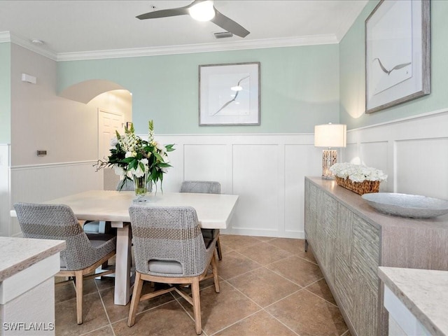 tiled dining area with ceiling fan and ornamental molding