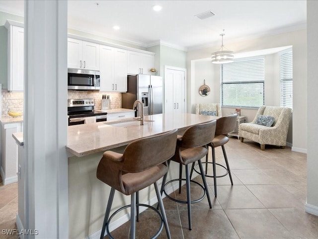 kitchen featuring a breakfast bar, sink, white cabinetry, hanging light fixtures, and appliances with stainless steel finishes