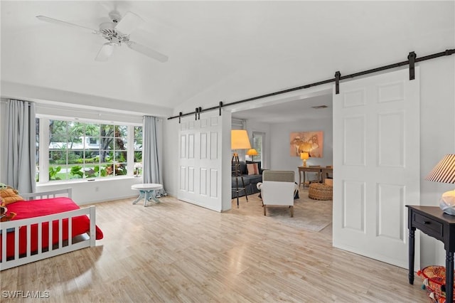 bedroom with ceiling fan, a barn door, light wood-type flooring, and vaulted ceiling