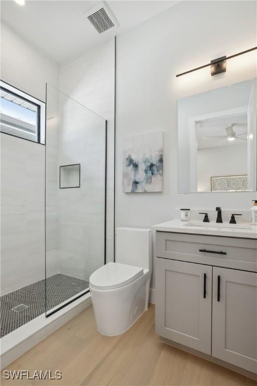 bathroom with toilet, tiled shower, hardwood / wood-style floors, and vanity