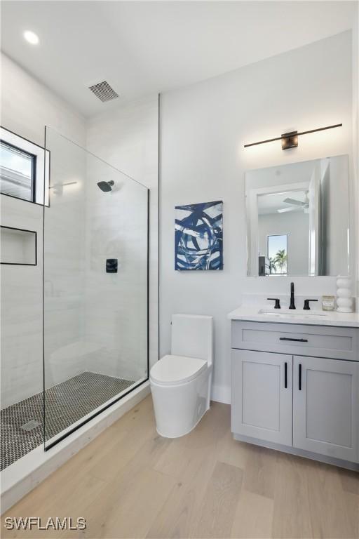 bathroom with toilet, vanity, wood-type flooring, and a shower with door