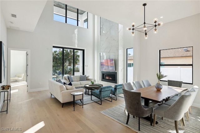 dining room featuring light wood-type flooring, a towering ceiling, a tile fireplace, and an inviting chandelier