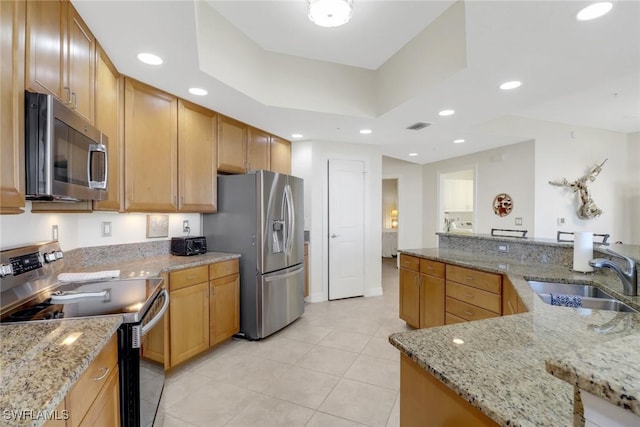 kitchen with stainless steel appliances, sink, light stone counters, and a tray ceiling