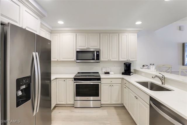 kitchen featuring stainless steel appliances, sink, white cabinetry, light wood-type flooring, and kitchen peninsula