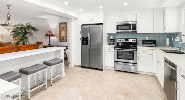 kitchen featuring tasteful backsplash, sink, hanging light fixtures, appliances with stainless steel finishes, and white cabinets