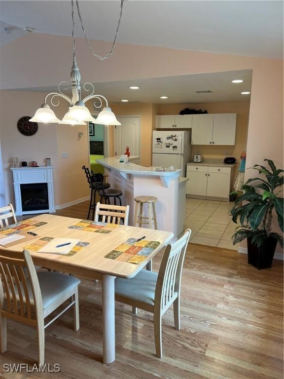 dining space featuring an inviting chandelier, vaulted ceiling, and light hardwood / wood-style flooring