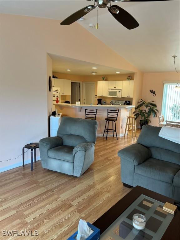 living room with ceiling fan, vaulted ceiling, and light hardwood / wood-style flooring