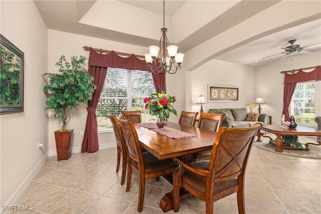 tiled dining space featuring a healthy amount of sunlight, ceiling fan with notable chandelier, and a tray ceiling