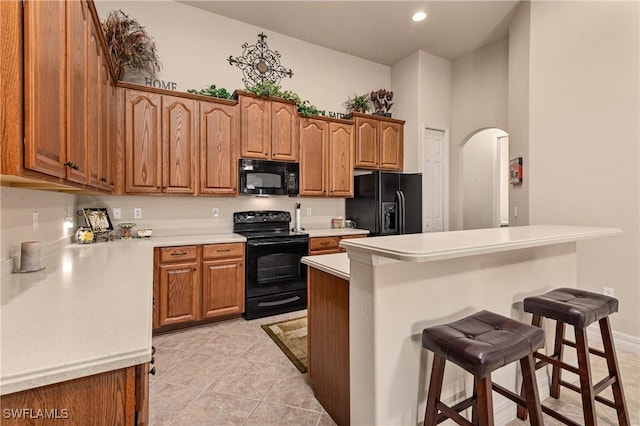 kitchen with a breakfast bar, a high ceiling, black appliances, light tile patterned flooring, and kitchen peninsula