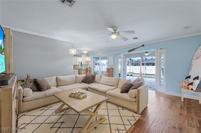 living room featuring ornamental molding, ceiling fan, light wood-type flooring, and a textured ceiling