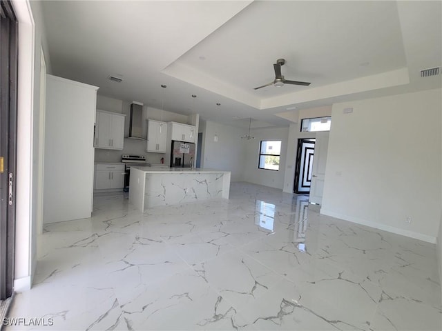 kitchen featuring stainless steel appliances, a tray ceiling, wall chimney exhaust hood, and white cabinetry